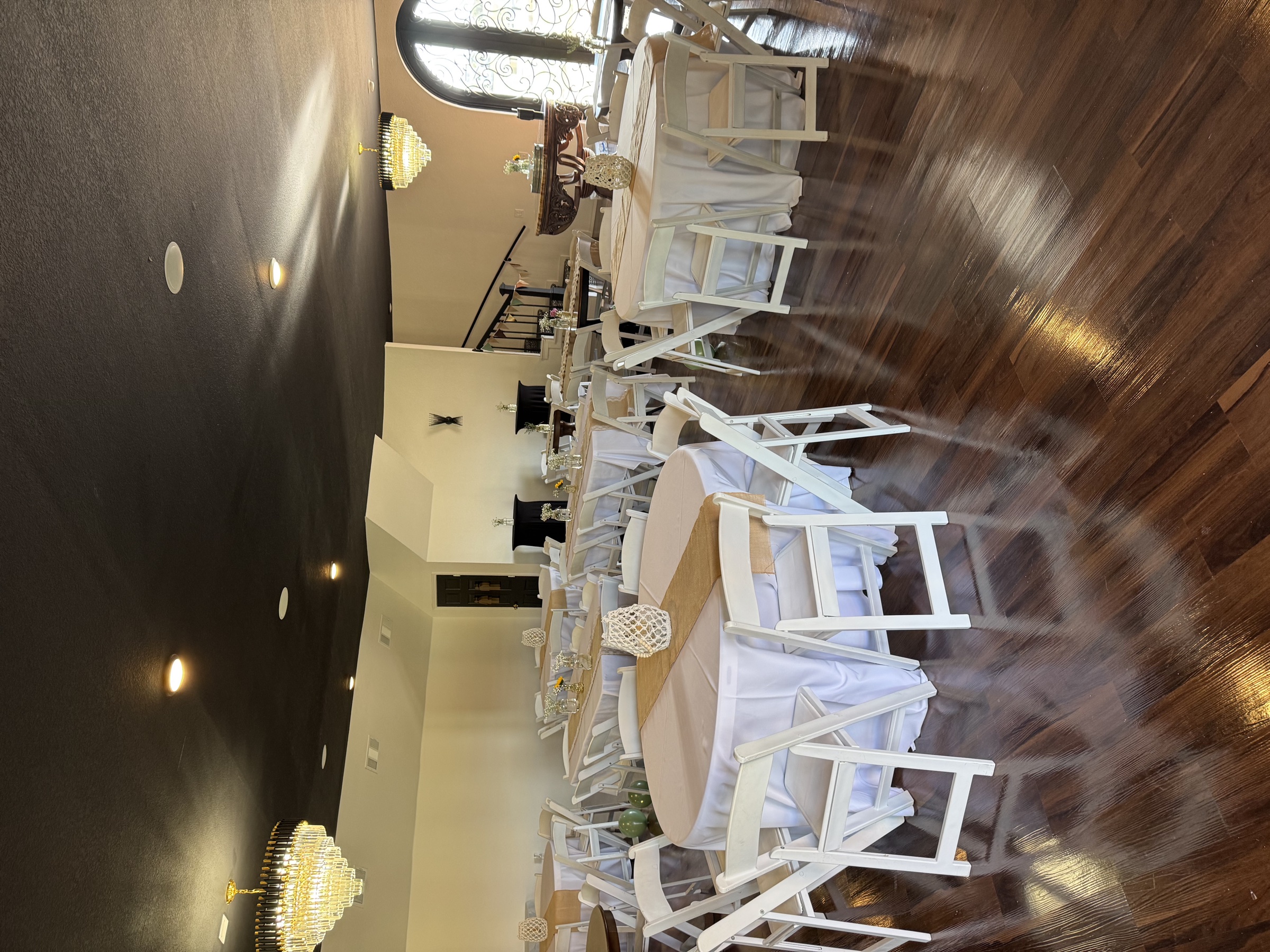 The venue interior with crystal chandeliers, round tables in cream linens with burlap runners, and a stained-glass arched doorway.