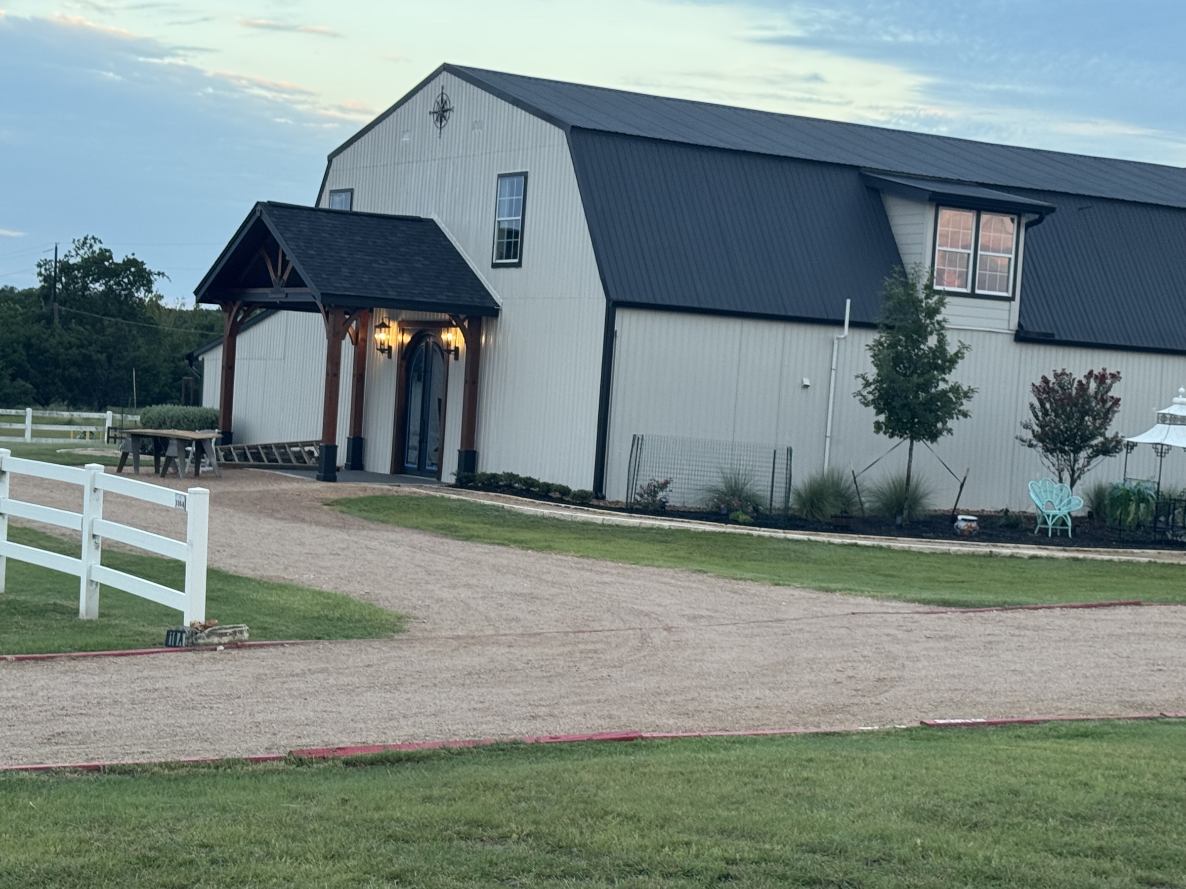 The barndominium exterior with covered portico entrance — daytime, ready for arriving guests.
