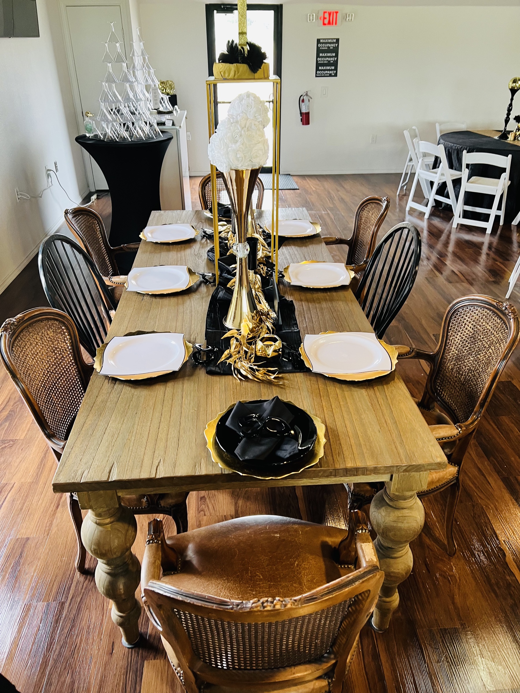 A long farmhouse table with cane chairs, a gold sequin runner, and stem candle holders set for an intimate wedding dinner.